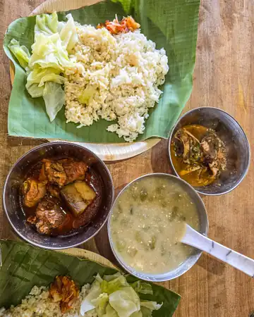 Rice, cabbage and two curries with a bowl of soup, served on banana leaves on a wooden table