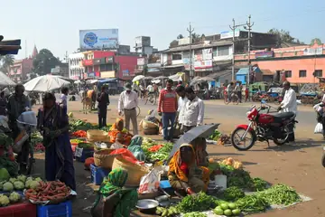 A roadside market where women sit on the ground with heaps of green beans, cauliflowers and carrots, and shoppers walk past