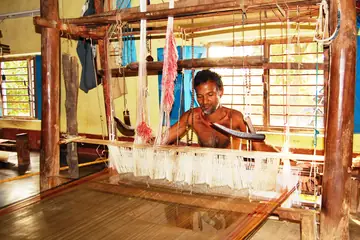 A weaver at a wooden handloom with white warp threads stretched in front of him, Sonepur