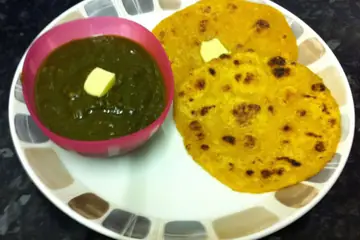 Two makki di roti with white butter beside a bowl of green sarson saag with butter on a plate