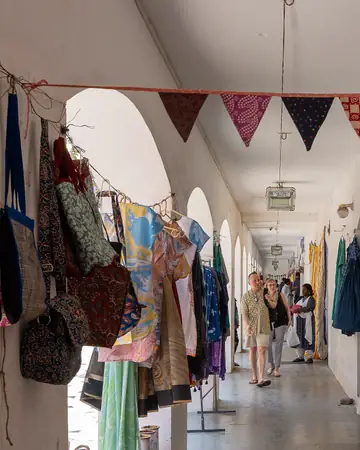 A whitewashed arcade with bunting of patchwork cloth, bags and clothes hanging at the shop fronts