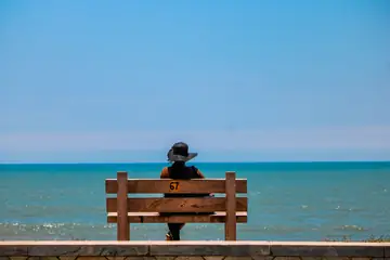 கடற்கரையில் மரப் பெஞ்சில் அமர்ந்து கடலைப் பார்க்கும் ஒருவர்
