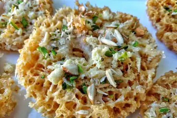 Round honeycomb ghewar sweets topped with sliced almonds and pistachio