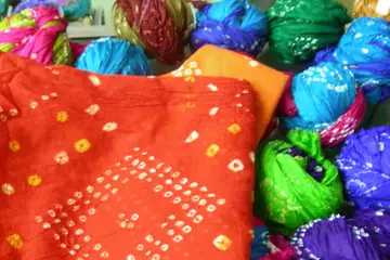 An orange bandhani cloth beside bundles of green, blue and purple turban cloths