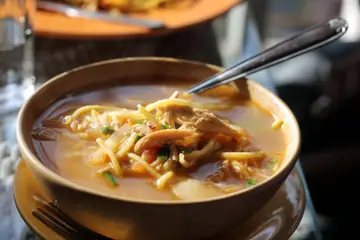 A brown bowl of thukpa, noodle soup with shredded meat, with a spoon in it