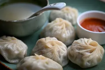 A plate of steamed momos with a small bowl of red chutney