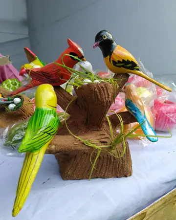 Hand-painted wooden parrots and small birds in red, green and yellow on a wooden branch stand