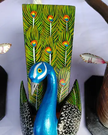 A hand-painted wooden peacock in blue and green with a patterned tail