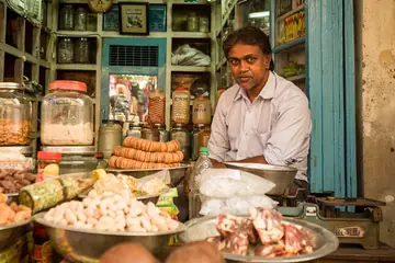 A shop owner sitting behind his counter among jars and bowls of nuts, dried fruit and spices in Hyderabad