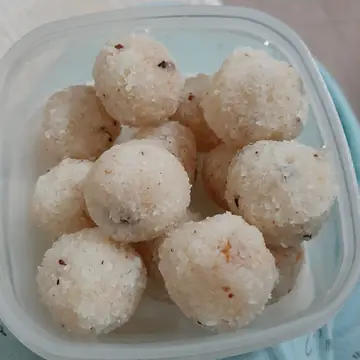 Round coconut laddus piled in a clear plastic box in Agartala