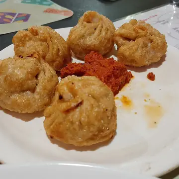 Five fried momos on a white plate with a spoon of red chutney in Agartala