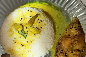 Fried hilsa fish beside a mound of rice in yellow mustard gravy on a steel plate in Agartala