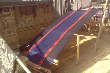 ধলাইয়ের গণ্ডাছড়ায় বাঁশের বেড়ার ঘরের সামনে নীল আর লাল সুতোয় টানা একটা কোমর-তাঁত