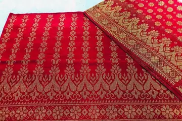 সোনালি রঙের ফুল-পাতার পাড় বোনা, ভাঁজ করা লাল রিগনাই কাপড়
