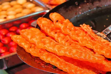 Freshly fried orange jalebi lifted on a slotted spoon above the pan