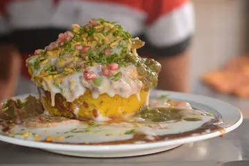 A plate of chaat topped with curd, chutney, sev and pomegranate seeds