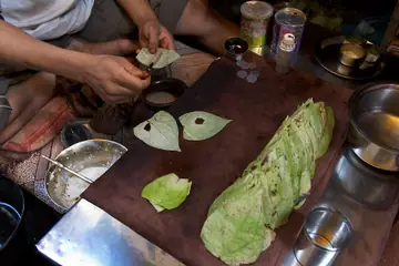 Hands spreading paste on a betel leaf at a paan seller's board in Varanasi, with more leaves stacked beside