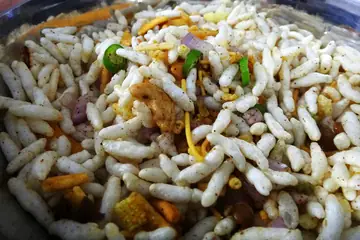 A steel bowl of spiced puffed rice mixed with chopped onion, green chilli and carrot