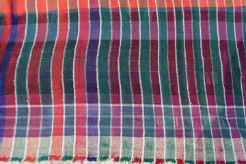 Handwoven cloth in red, green, blue and white stripes with a fringed edge, laid flat