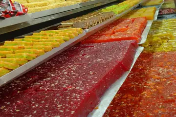 Long trays of red, yellow and orange barfi sweets in rows behind the glass of a sweet shop in Kolkata