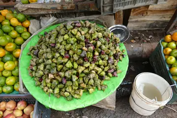 A green plate heaped with water caltrops at a Burrabazar stall in Kolkata, with oranges and apples on both sides