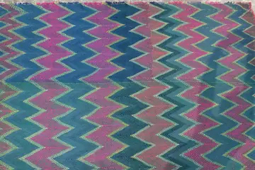 A quilted cloth stitched in zigzag rows of pink, teal and blue thread