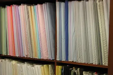 Bolts of pastel and white suit fabric standing on wooden shelves