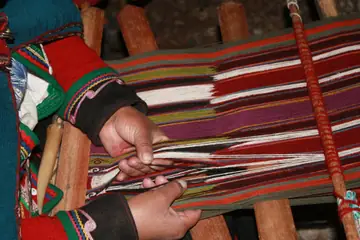 Hands weaving a striped woollen band on a wooden loom