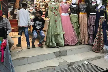 Mannequins dressed in ready-made lehenga and gown outfits at a shop front, with stacked cloth inside