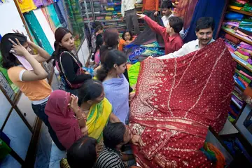 A shopkeeper holding up a red embroidered sari for a group of women customers in a fabric shop in Varanasi