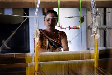 A weaver at a handloom strung with yellow silk threads