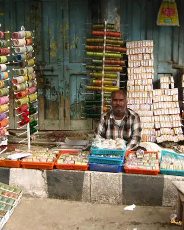 A bangle seller sitting at his stall between racks of bangles and boxes of bindi packs