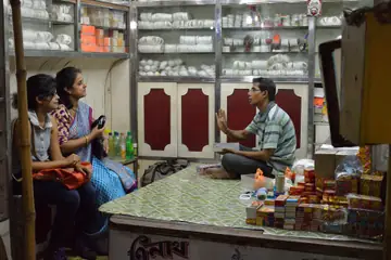കൗണ്ടറിൽ ഇരുന്ന് രണ്ടു സ്ത്രീ കസ്റ്റമർമാർക്ക് ശംഖുവളകൾ കാണിക്കുന്ന ഒരു കടക്കാരൻ