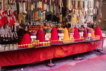 A stall with red kumkum heaps on a red cloth under hanging bead necklaces