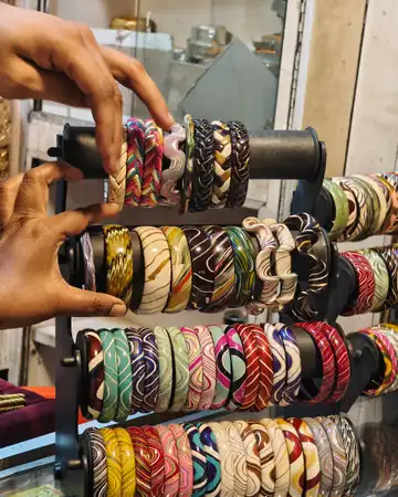 Hands sliding patterned lac bangles along a rack in a bangle shop in Hyderabad