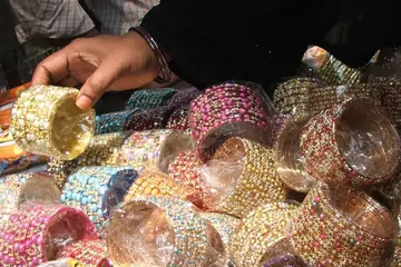 A hand lifting a pearl-studded bangle from a heap of sparkling bangles in Hyderabad