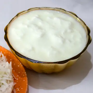 A glass bowl of thick white curd beside a plate of rice