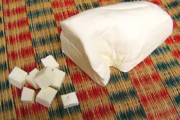 A block of fresh paneer and cut cubes on a woven mat
