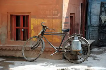 A milkman's bicycle with a steel milk can, parked by an orange wall