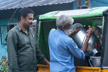 A milkman pouring milk from a big steel can while a customer stands beside him at Thodupuzha, Kerala