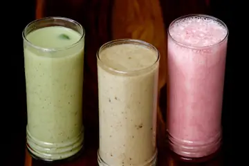 Three tall glasses of mint, plain and rose lassi against a dark background