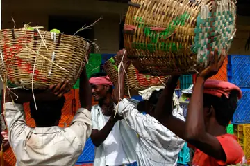 മൊത്തവിപണിയിൽ സാധനങ്ങൾ നിറച്ച വലിയ മെടഞ്ഞ കുട്ടകൾ തലയിലേക്ക് ഉയർത്തുന്ന ചുമട്ടുതൊഴിലാളികൾ