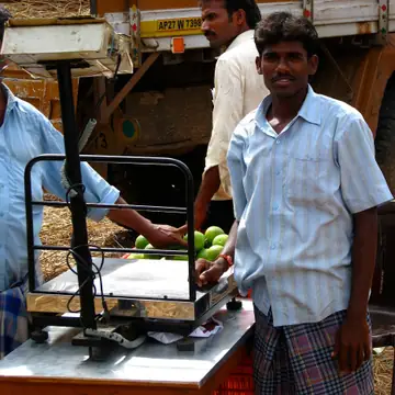 A trader smiling beside a large floor scale as goods are weighed next to a lorry