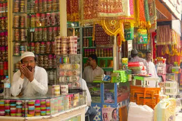A shop owner resting his chin on a glass counter of bangles, with more bridal-ware shops side by side