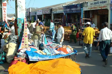 A row of shops behind cloth stalls on a sunny market street with shoppers