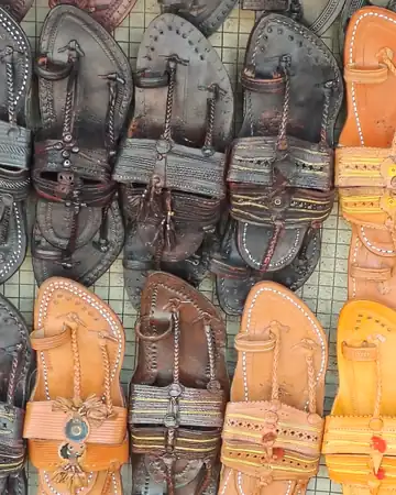 Black and tan chappals hung in rows on a wire mesh