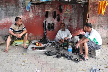 Three cobblers sitting at their pavement spot with shoes and tools laid out