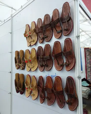 Pairs of tan and brown Kolhapuri chappals hung in rows on a white display wall