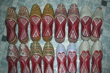 Pairs of red and gold embroidered juttis laid out in two rows on a tiled floor