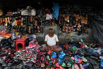 A footwear seller sitting among heaps of chappals and slippers